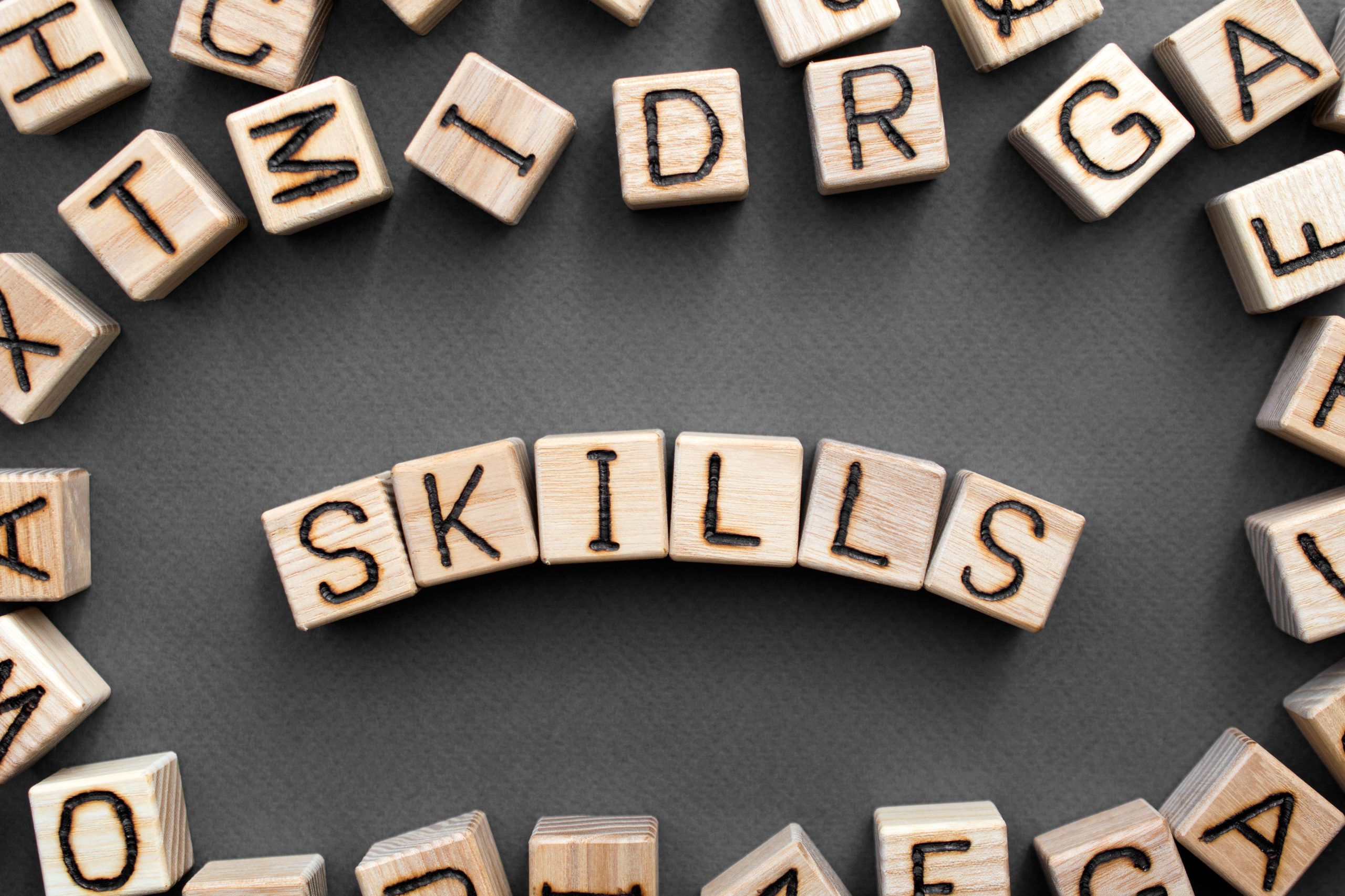 the word skills wooden cubes with burnt letters, skill acquisition, gray background top view, scattered cubes around random letters